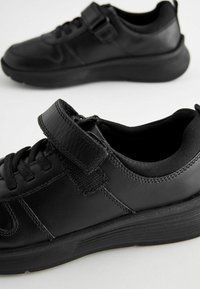 Zwarte sportieve schoenen van leer met een gestructureerde afwerking, voorzien van een klittenbandsluiting, ronde neus en een duurzame rubberen zool.