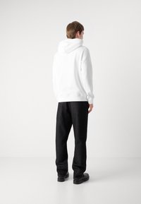 Sudadera blanca con capucha de textura suave, combinada con pantalones oscuros y de corte holgado. El diseño es simple y minimalista, sin patrones.