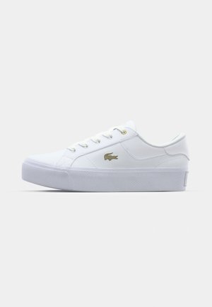 White low-top sneaker with thick sole, metal eyelets on laces, and gold crocodile logo on side.