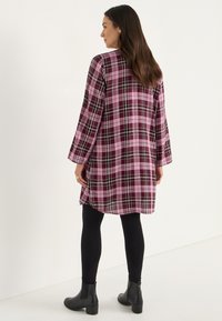 Pitkähihainen ruudullinen mekko purppura, vaaleanpunainen ja musta väri; rento malli, jossa helma ulottuu polven ylle; yhdistetty mustiin legginsseihin ja nilkkureihin.