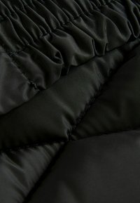 Tissu noir matelassé présentant une texture froncée, une surface lisse et des coutures contrastées, affichant un design léger mais durable.