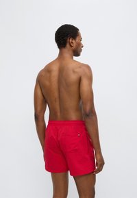 Κόκκινα μαγιό σορτς με ελαστική μέση και πίσω τσέπη. Ελαφρύ ύφασμα, μήκος πάνω από το γόνατο, με απλό, μονόχρωμο σχέδιο.