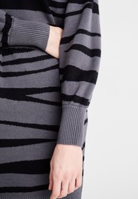 Gebreide jurk in grijs met zwarte zigzagstrepen. Heeft geribbelde manchetten en een ontspannen ontwerp. Zachte textuur en warm materiaal.