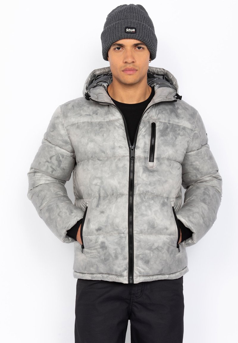 Grå pufferjakke med marmormønster, sort lynlås, fast hætte og to sidelommer, båret over en sort skjorte og parret med en strikket hue.