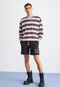 Camisa de manga larga a rayas en rosa y negro, combinada con pantalones cortos negros con un diseño de calavera. Llevada con botas negras de cordones hasta el tobillo.