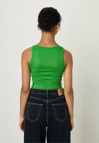 Žalia prigludusi marškinėlių viršutinė su raštuota tekstūra, derinama su juodomis džinsinėmis kelnėmis su aukštu liemeniu, turinčiomis odinį etiketę ir dviem užpakalinėmis kišenėmis.