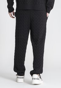 Zwarte gebreide pantalon met een gestructureerd kabelpatroon. Elastische tailleband met zijzakken, gecombineerd met witte sneakers met merknaam.