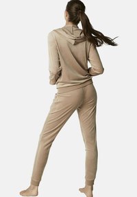 Ensemble de loungewear en velours de couleur beige clair, comprenant un haut à capuche et un pantalon slim avec des poignets côtelés et une texture lisse.