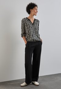 Blusa a righe bianco e nera con scollo a V e maniche arrotolate, abbinata a pantaloni neri a vita alta e sneakers bianche. Texture liscia.