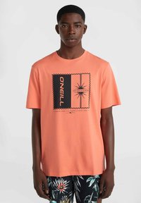 Camiseta coral de manga corta, con un diseño gráfico en blanco y negro, texto e ilustración de palmera. Combinada con unos pantalones cortos de estampado floral.