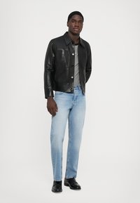 Sort læderjakke med krave og brystlomme, parret med en grå T-shirt og lyseblå jeans. Sorte sko fuldender looket.