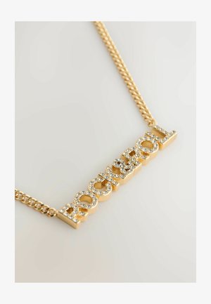 Złocony naszyjnik z wyrazem "ROCK" w wyraźnych literach, zdobiony przezroczystymi cyrkoniami. Skręcony wzór łańcuszka dodaje tekstury.