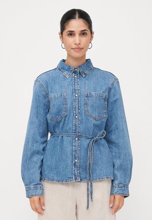 Camisa de ganga azul com botões, de mangas longas, duas bolsos no peito e um cinto correspondente à cintura, apresentando costuras em contraste.