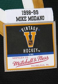 Label on hockey jersey showing "1998-99 Mike Modano" and vintage Mitchell & Ness NHL logo patch with "Philadelphia, PA" text.