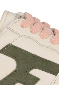 Zapatillas color beige claro con acentos de ante verde, cordones texturizados en rosa y costuras en contraste. Diseño curvado y logo embebido son características destacadas.