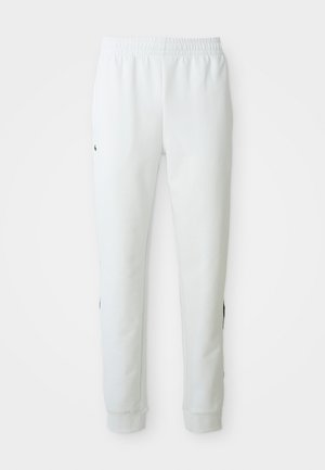 Witte sportbroek met een elastische tailleband, taps toelopende pijpen en zwarte accenten aan de zijkanten. Gemaakt van zachte, gestructureerde stof.
