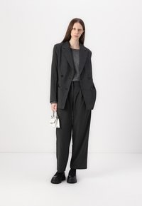 Blazer double boutonnage gris à rayures avec un pantalon à jambes larges. Haut gris simple, chaussures noires épaisses et un petit sac à main blanc.
