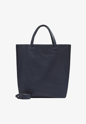 Granatowa skórzana torba na ramię z dwiema rączkami i odpinanym paskiem na ramię położona obok na białym tle.