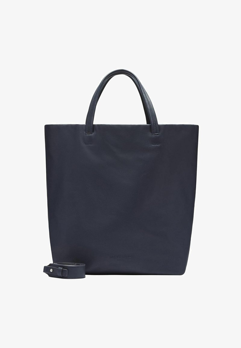 Granatowa skórzana torba na ramię z dwiema rączkami i odpinanym paskiem na ramię położona obok na białym tle.