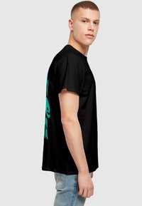 Sort kortærmet t-shirt med et stort turkist grafisk design på ryggen. Materialet ser glat ud og har en afslappet pasform.