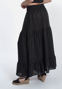 Zwarte tiered maxi rok van lichtgewicht stof met een smock taille. Heeft een gerimpelde zoom en wordt gedragen met espadrille plateformes.