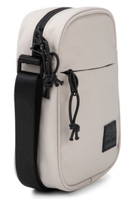 Borsa a tracolla in tela beige con cerniera nera, tracolla regolabile, tasca frontale e piccolo patch in pelle; forma rettangolare, texture liscia.