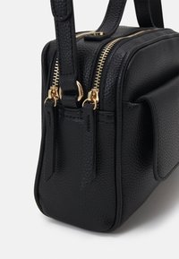 Sac en cuir noir à texture grainée, doté de deux fermetures éclair dorées, de deux poignées supérieures et d'une poche latérale avec rabat.