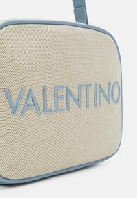 Beige rektangulär väska med en texturerad yta, med en blå broderad "VALENTINO"-logotyp och kantade kanter i en matchande färg.