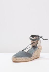 Šedé plátěné espadrilky na klínu s jutu rope podpatkem, kotníkovými šňůrkami a plochým pleteným kotníkovým páskem. Obsahují špičatou špičku a texturovanou stélku.