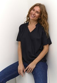 Mörkblå kortärmad blus med v-ringning och rynkning vid halslinningen. Slät textur, kombinerad med mörkblå jeans.