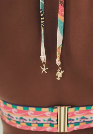 Rückansicht einer Person, die einen bunt gemusterten Bikini trägt, an dessen Bändchen goldene Seesterne und Hummer-Anhänger hängen.