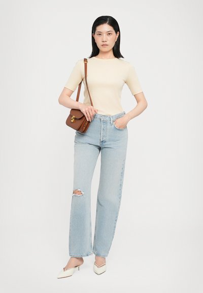 Beige short-sleeve top, high-waisted light blue jeans with a ripped knee, brown crossbody bag, and cream pointed-toe heels.