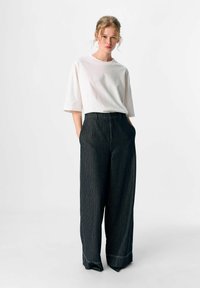 Weißes Baumwoll-T-Shirt mit kurzen Ärmeln, kombiniert mit dunkel gestreiften weit geschnittenen Hosen mit hoher Taille und dezenten Saumdetails.