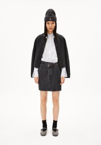 Chaqueta corta de mezcla de lana oscura, camisa blanca con cuello, falda de mezclilla negra y zapatos de deslizar negros con tachuelas, junto con calcetines. Diseño minimalista.