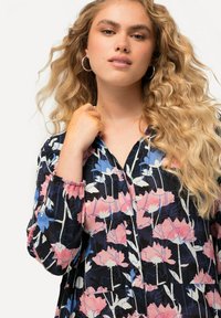 Musta paita, jossa on vaaleanpunaisia ja sinisiä kukkakuoseja, pitkät hihat elastisilla hihoilla, napitus edessä, kevyt kangas ja hienovarainen rakenne.