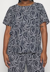 Mörkblå kortärmad topp med ett vitt abstrakt mönster. Mjuk textil med en avslappnad passform, rund halsringning och flödande design.