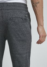 Grey, textured jogger pants with a back pocket and branded tag. Elastic waistband for comfort. Visible stitching details.