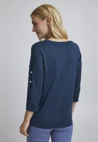 Marineblauer Strickpullover mit Dreiviertelärmeln, dekoriert mit Knopfakzenten an den Ärmelbündchen sowie einem gerippten Saum und Bündchen. Weicher Griff.