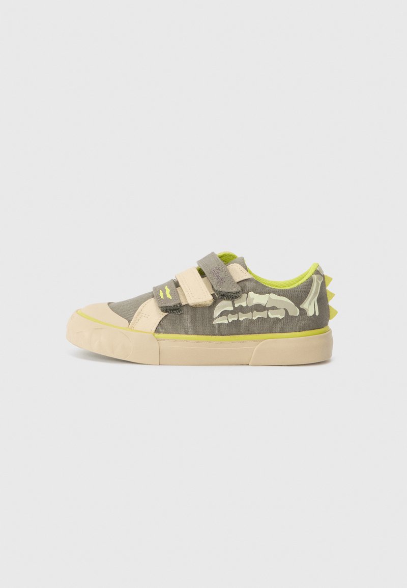 Sneaker na rzepy z szarym płótnem, kremową osłoną na palce, neonowozielonymi akcentami oraz graficznym motywem w kształcie kości na boku. Podeszwa jest teksturowana.
