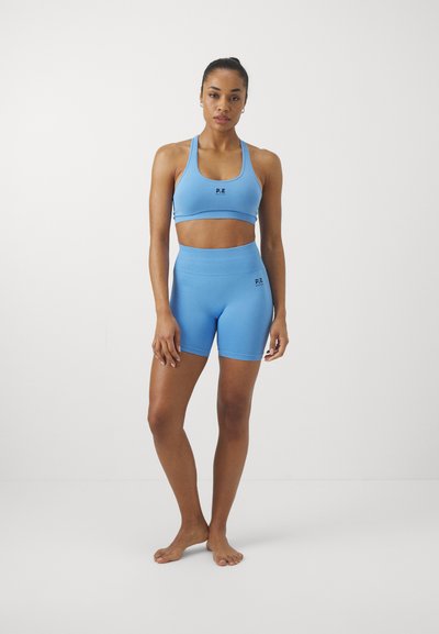 Sutiã desportivo azul e calções de cintura alta feitos de tecido elástico, com textura ribada e detalhe do logótipo na parte da frente.