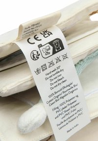 Étiquette de vêtement montrant les marques CE UKCA, symboles de lavage, instructions de lavage à la main à 30°C, détails du matériau en plusieurs langues, attachée à un article en tissu.