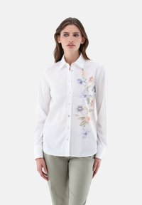 White button-up shirt with a floral design in pastel colors on the left side. Long sleeves and a standard collar, made from smooth fabric.