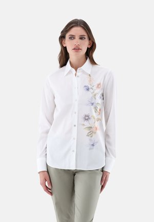 White button-up shirt with a floral design in pastel colors on the left side. Long sleeves and a standard collar, made from smooth fabric.