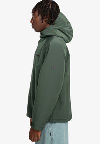 Green, lightweight jacket with a hood, textured fabric, zippered chest pocket, and a logo detail on the sleeve. Side view shown.