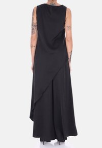 Abito nero senza maniche con design drappeggiato, caratterizzato da un orlo asimmetrico e dettagli a chiave sulla schiena. Tessuto liscio, taglio fino al pavimento.