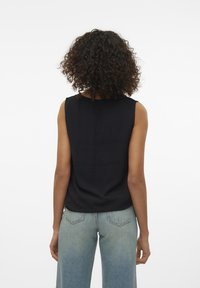 Black sleeveless top with textured fabric, round neckline, and relaxed fit. Paired with light blue wide-leg jeans.