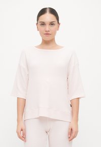 Gaiši rozā, brīva piegriezuma īsām piedurknēm blūze ar ribotu faktūru un plašu kakla izgriezumu. Apvienota ar atbilstošām gaiši rozām biksēm.