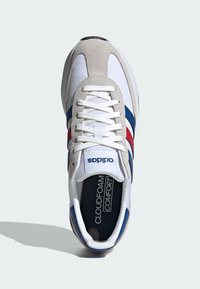 Baskets blanches avec des accents en suède gris, des rayures rouges et bleues, et une semelle intérieure noire étiquetée "CLOUDFOAM COMFORT". Elles possèdent des lacets et un bout rond.