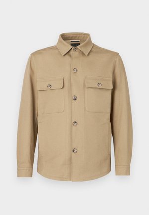 Casaco bege feito de tecido, com fecho frontal de botões, gola em bico, dois bolsos no peito e mangas compridas com punhos de botão.