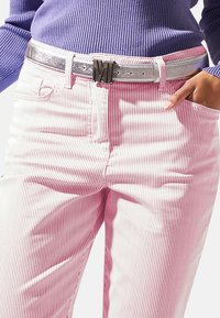 Horizontaal gestreepte roze en witte broek met een zilveren metallic riem met een gedurfde, zwarte sluiting. De top is gemaakt van ribbelig paars materiaal.